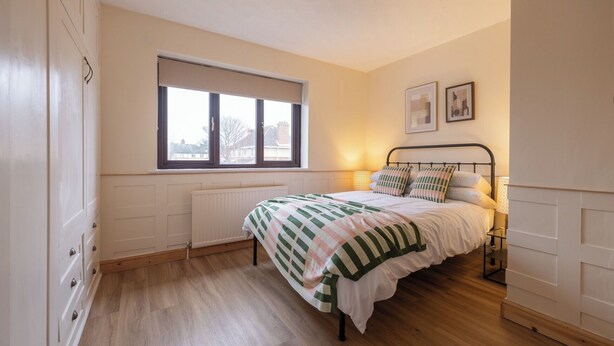 Un dormitorio con cama, ventana, radiador y una lámpara fijada a la pared.