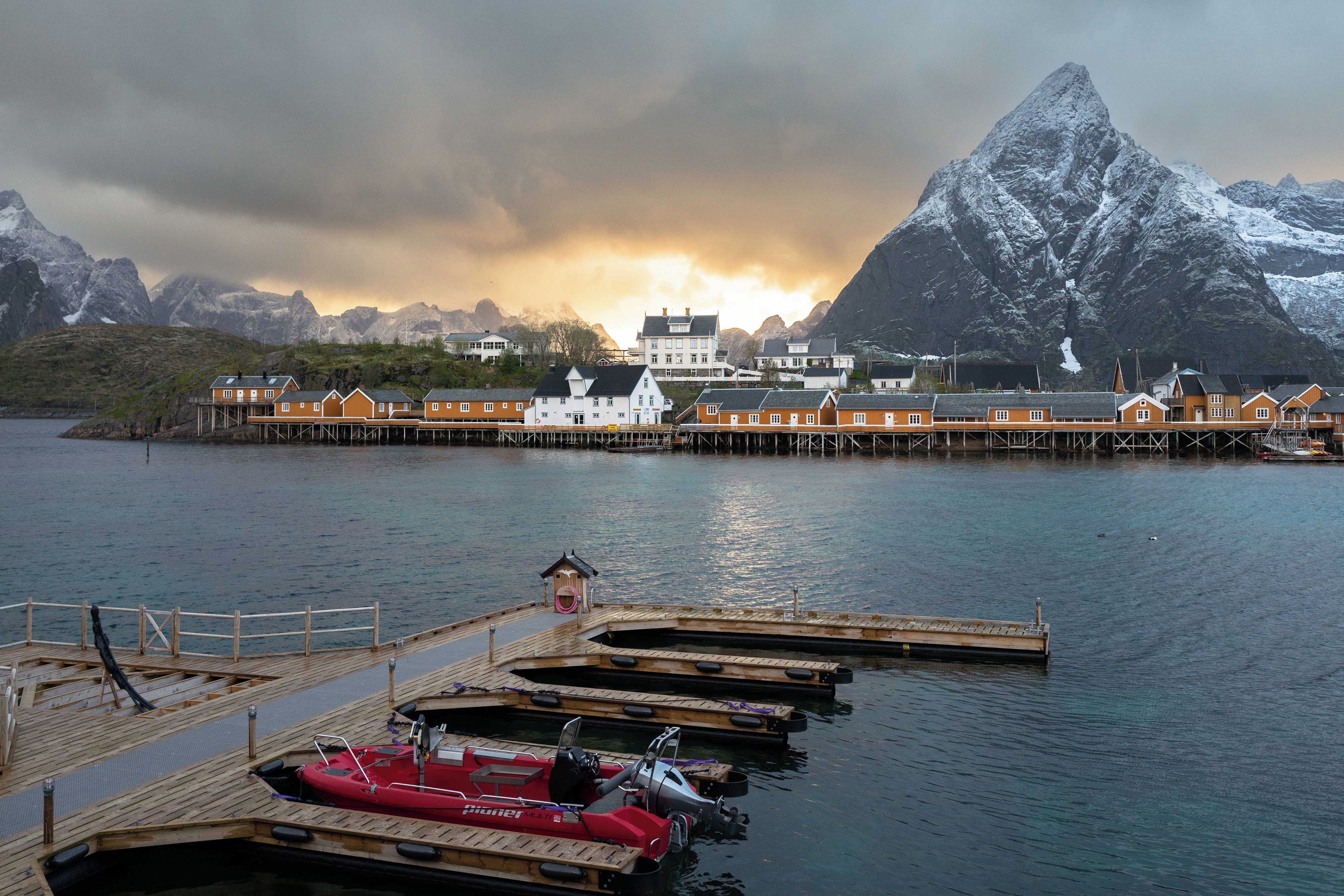 A coastal town with a pier, boats, and a mountain in the background.