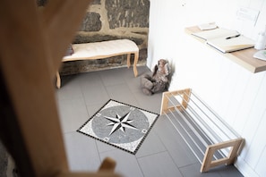 A room with a stone wall, a bench, a small table with a notebook, a decorative squirrel sculpture, and a floor with a compass design. - Sakrisøy Gjestegård-Solbakken anno 1880 (Nordland)