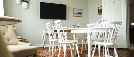 A dining area with a white table and chairs, a flat-screen TV mounted on the wall, and a patterned rug on the floor.