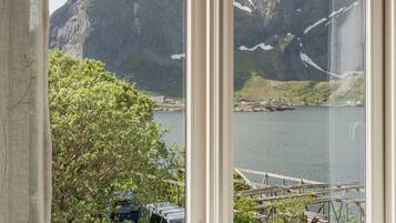 A window with a view of a mountainous landscape, a body of water, and a dock with boats.