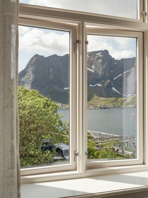 A window with a view of a mountainous landscape, a body of water, and a dock with boats.