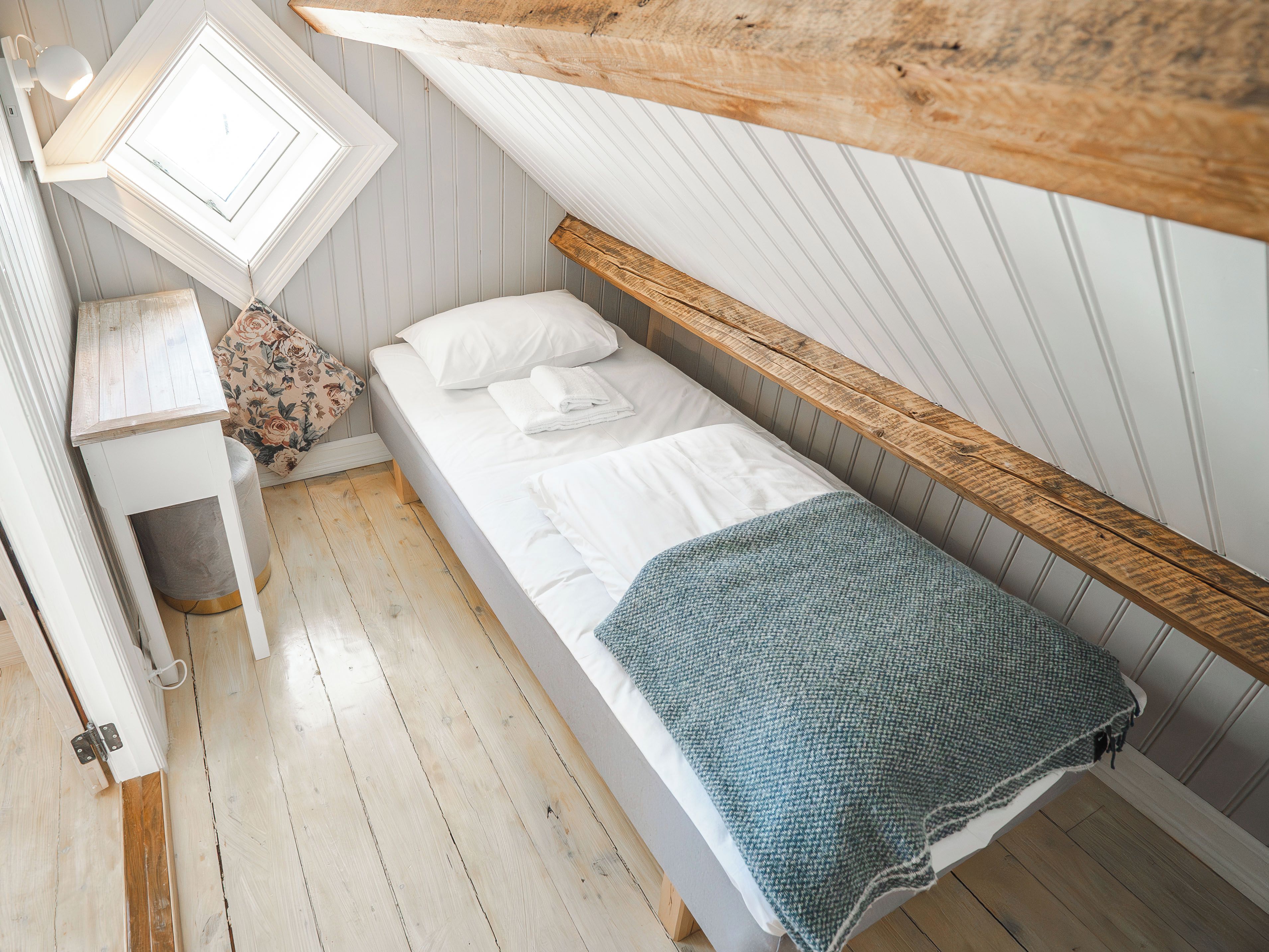 A small, single-bed room with a wooden headboard, a bedside table, a lamp, and a window.