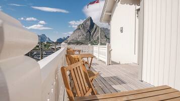 A deck with wooden chairs and tables, overlooking a mountainous landscape with a flag.