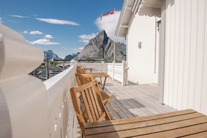 A deck with wooden chairs and tables, overlooking a mountainous landscape with a flag.