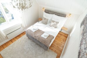 A bedroom with a bed, bedside tables, a chandelier, and a window.
