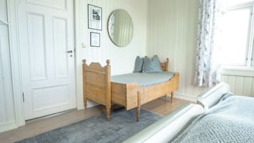 A bedroom with a wooden bed, a door, a mirror, and a window with curtains.