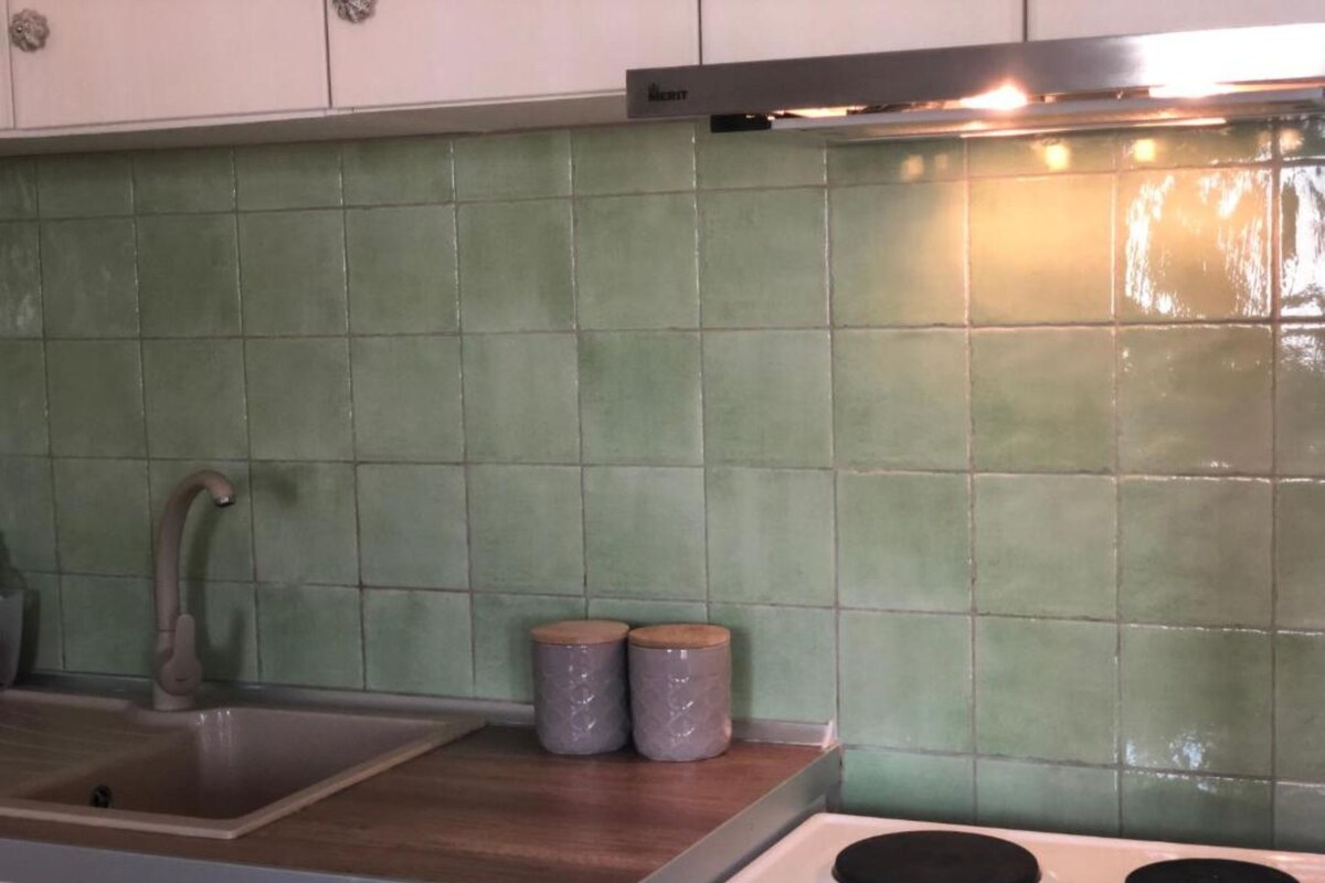 A kitchen with a sink, two burners, and a green tiled backsplash.