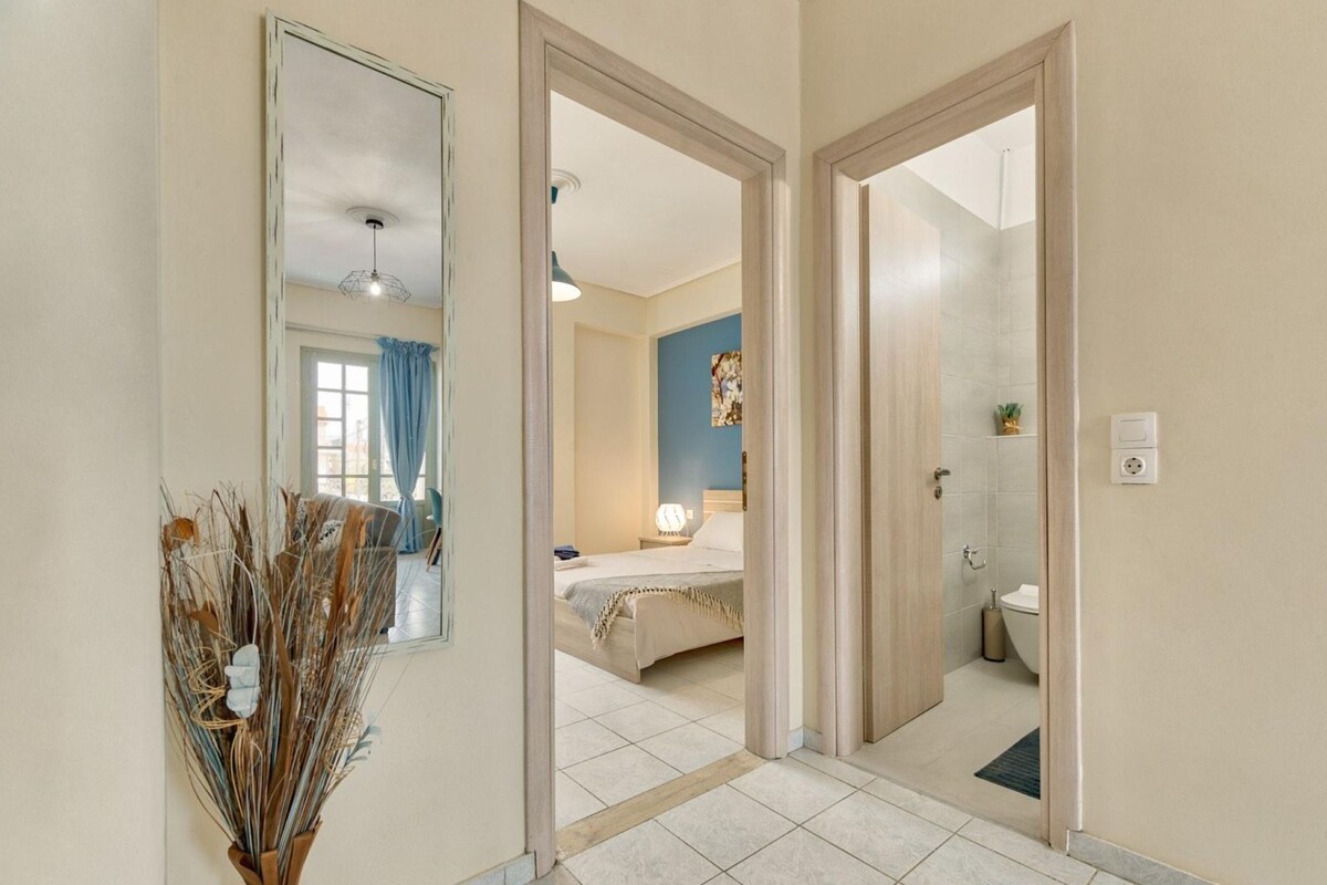A hotel room with a bed, a bathroom with a toilet and sink, a mirror, and a vase with dried plants.