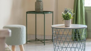 Ein Zimmer mit einem runden Metalltisch, einem kleinen Hocker, einem Blumentopf und einer dekorativen Glasvase auf einem kleinen Tisch.