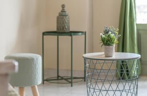 A room with a round metal table, a small stool, a potted plant, and a decorative jar on a small table.