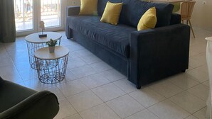 Ein Wohnzimmer mit einer Couch, einem kleinen runden Tisch, einem Sessel, einem Deckenventilator, einem Fenster und einer Wandklimaanlage.