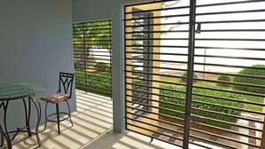A balcony with a glass table and chairs, a view of a garden, and a metal gate.