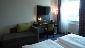 Habitación de hotel con cama, escritorio, silla, televisor y ventana con cortinas.