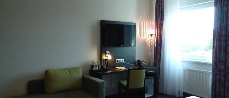 A hotel room with a bed, a desk, a chair, a TV, and a window with curtains.