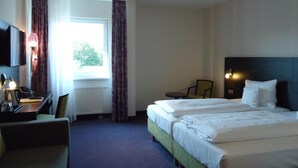 Habitación de hotel con dos camas, un escritorio con lámpara, una silla y vistas al exterior a través de una ventana.