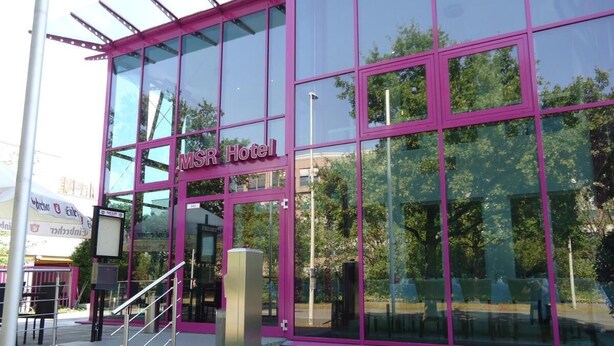 Un edificio moderno con grandes ventanales y un marco rosa, identificado como "MSR Hotel".