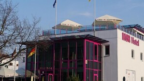Un edificio moderno con fachada de vidrio, una entrada destacada y banderas en la parte superior.