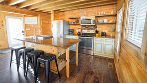 Cucina di una baita in legno con isola centrale, sgabelli da bar, frigorifero, microonde, fornello e lavandino.