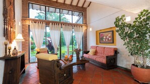 A cozy living room with a wooden sofa, a coffee table, and a large window with curtains. - Country house-Chalet in El Caimo, Armenia with private pool and BBQ (El Caimo)