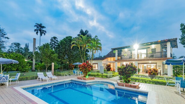 A pool area with lounge chairs, a well-maintained lawn, and a two-story house with a balcony. - Country house-Chalet in El Caimo, Armenia with private pool and BBQ (El Caimo)