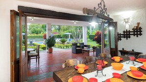 A dining area with a table set for a meal, a patio with outdoor seating, and a view of a garden. - Country house-Chalet in El Caimo, Armenia with private pool and BBQ (El Caimo)