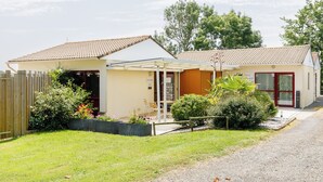 Ein zweistöckiges Haus mit Ziegeldach, einer Veranda und einem kleinen Gartenbereich mit Pflanzen und einer Bank.