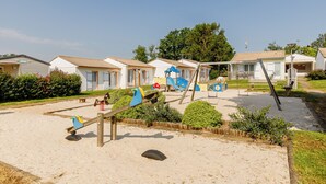 Ein Spielplatz mit Schaukeln und einer Wippe in einer sandigen Fläche, umgeben von Mobilheimen.