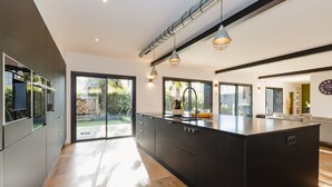 Une cuisine moderne dotée d’un grand îlot central, de meubles de rangement aux couleurs sombres et offrant une vue sur l’extérieur.