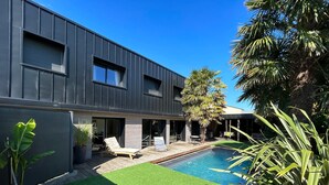 Une maison moderne dotée d’une piscine, d’un patio avec des chaises longues et d’un jardin bien entretenu.