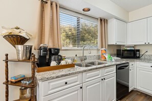 A kitchen with white cabinets, a granite countertop, a coffee maker, a microwave, and a window with blinds.
