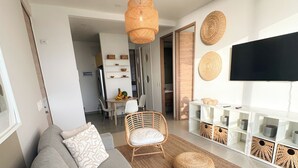 Un soggiorno moderno con un divano grigio, una poltrona in vimini e un televisore a schermo piatto montato a parete.