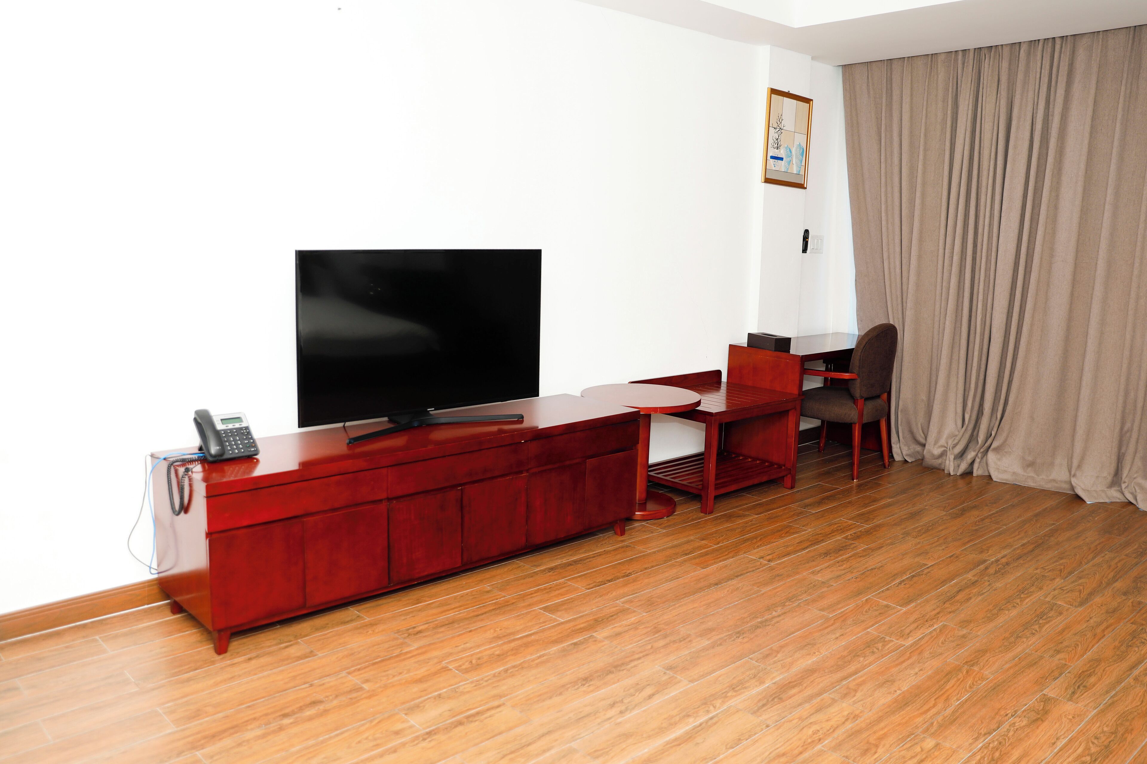 A room with a wooden floor, a red entertainment unit with a flat-screen TV, a telephone, and a small table with a chair.