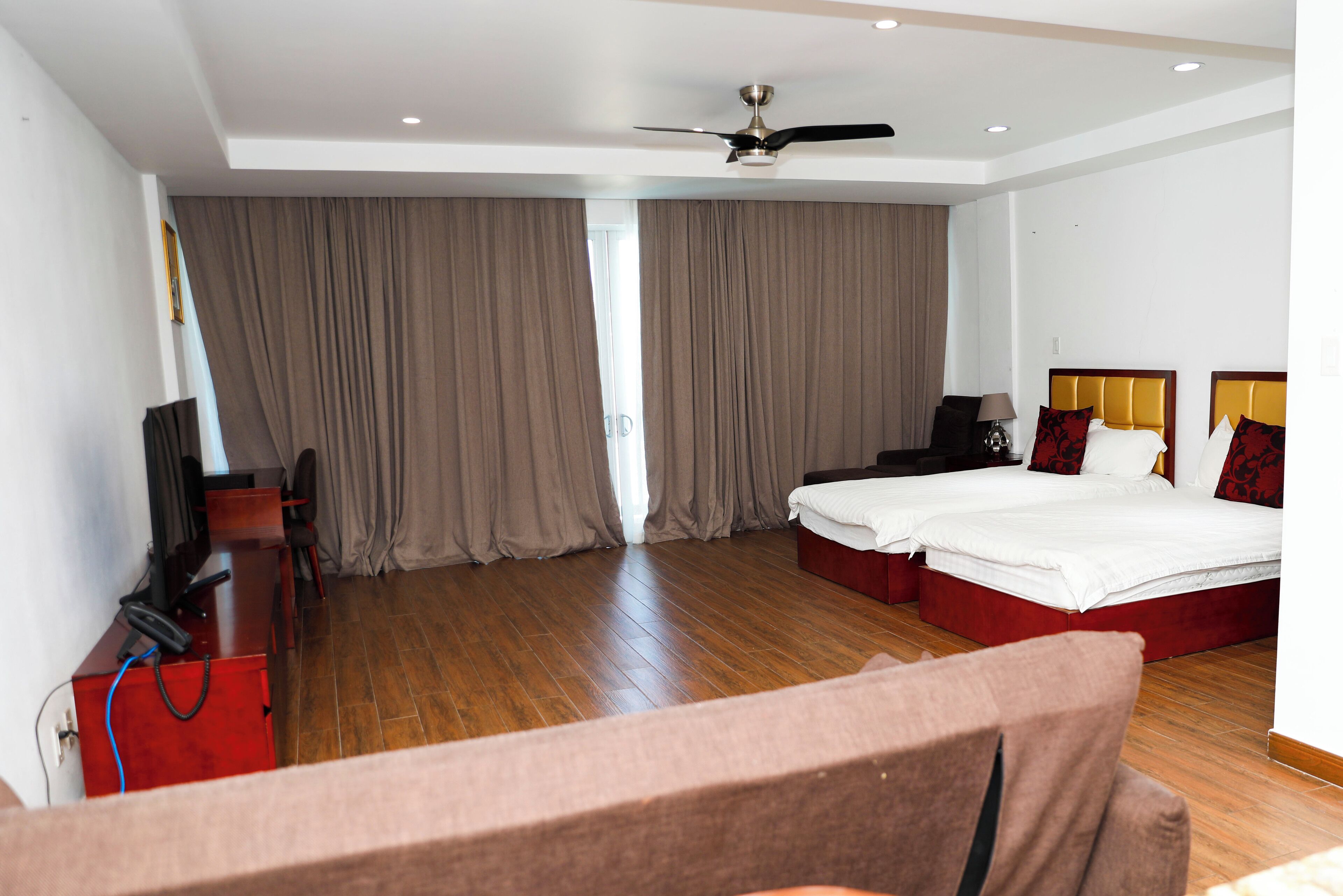 Una habitación de hotel con una cama, un escritorio, una silla, un televisor y un ventilador de techo.