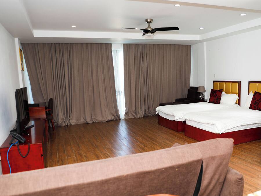 Una habitación de hotel con una cama, un escritorio, una silla, un televisor y un ventilador de techo.