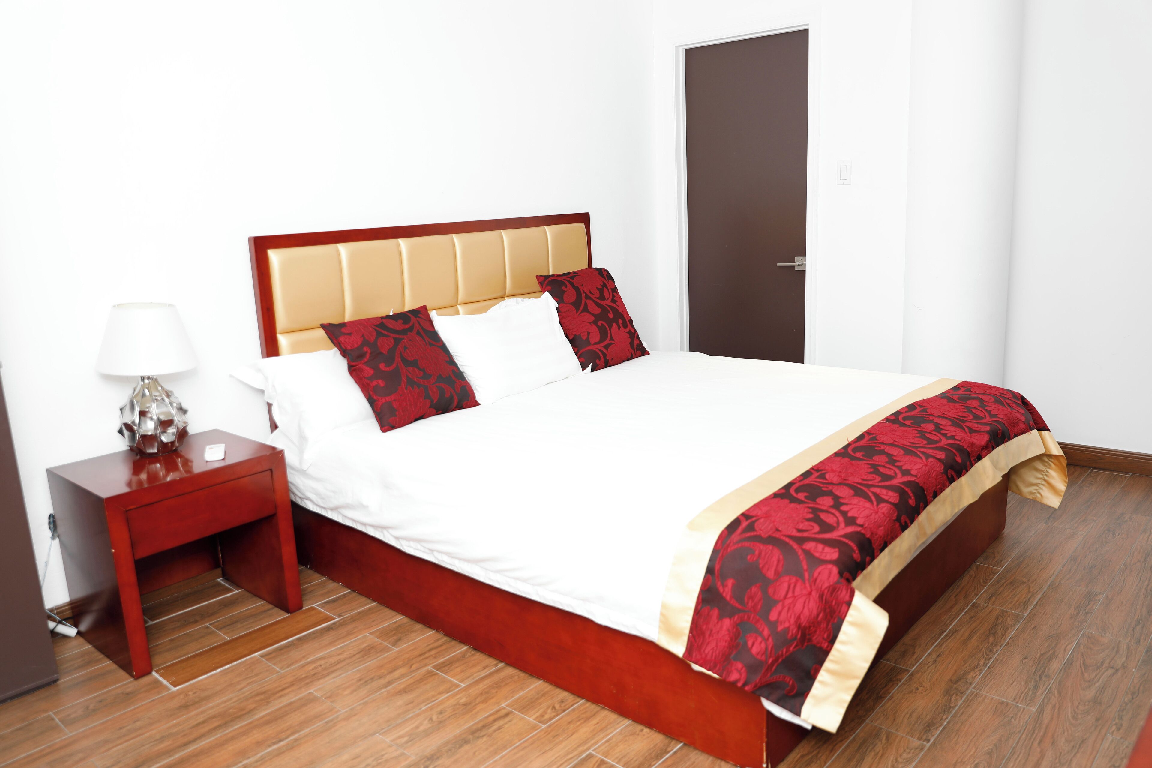 Un letto rifatto con cura, una testiera in legno, un comodino con una lampada e una porta sullo sfondo.