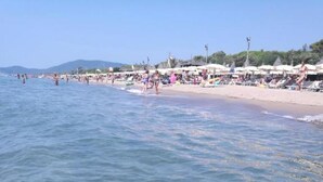 A beach with clear water, umbrellas, and people.