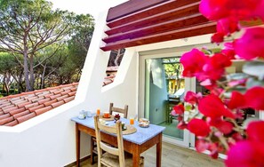 A dining area with a table set for two, a wooden pergola, and a view of a tiled roof and trees.