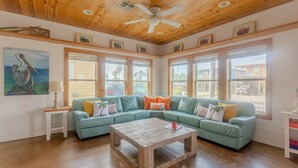 Un salon spacieux doté d’un plafond en bois, d’un canapé d’angle vert, d’une table basse en bois et de grandes fenêtres offrant une vue sur l’extérieur.