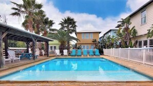 Une piscine avec des chaises longues, des palmiers et un espace salon abrité.