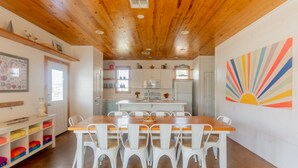 Une cuisine moderne avec des meubles blancs, un plafond en bois et une décoration murale colorée en forme de soleil rayonnant.