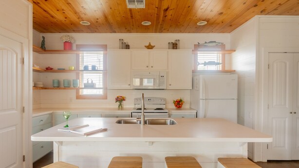 Une cuisine avec des meubles blancs, un îlot central doté de tabourets, un four à micro-ondes, une cuisinière et un réfrigérateur.