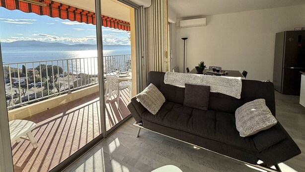 Un balcon avec vue sur la mer et les montagnes, un canapé avec des coussins, une table et un réfrigérateur.