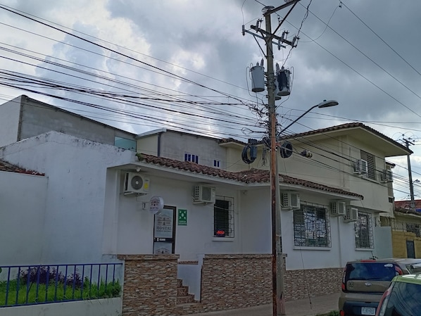 A two-story building with a white facade, a small porch, and multiple air conditioning units. - Hostal Mansión Histórica (Santa Ana)