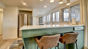 A modern kitchen with a central island, stainless steel appliances, and a large window providing natural light. - Golf Course Home on 10th - Newly Renovated (Millersburg)