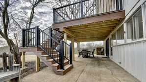 A covered patio area with a wooden staircase leading to a deck, a table with chairs, and a view of trees in the background. - Golf Course Home on 10th - Newly Renovated (Millersburg)