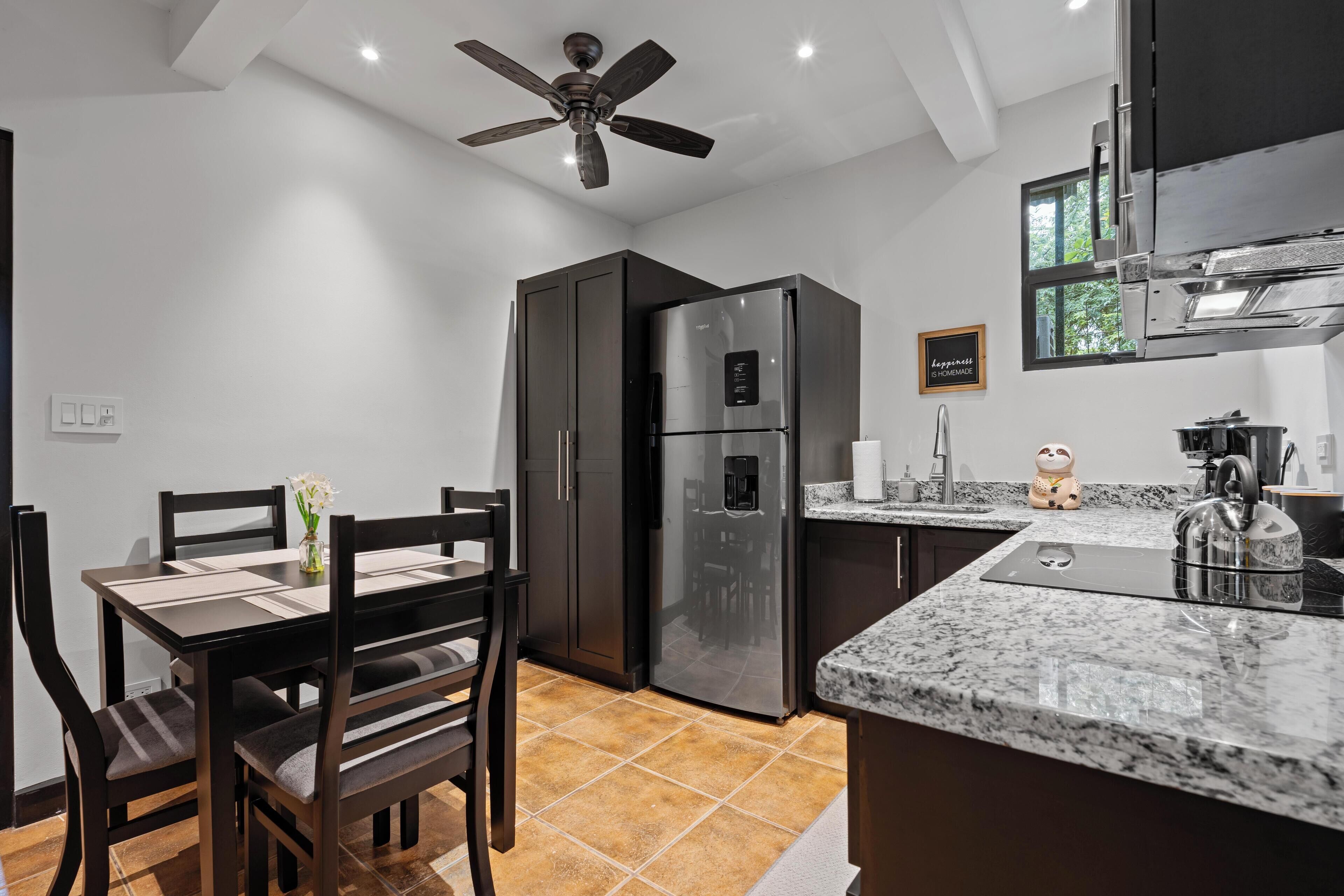 A modern kitchen with a built-in refrigerator, a dining table with chairs, a ceiling fan, and a window providing natural light.