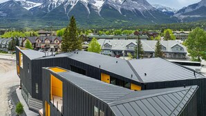 Ein modernes Gebäude mit geneigtem Dach, umgeben von Wohnhäusern und Bergen im Hintergrund.