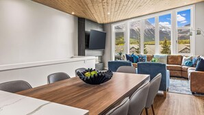 Ein modernes Wohnzimmer mit Holzboden, einem Essbereich mit Holztisch und einem großen Fenster mit Blick auf die Berge.