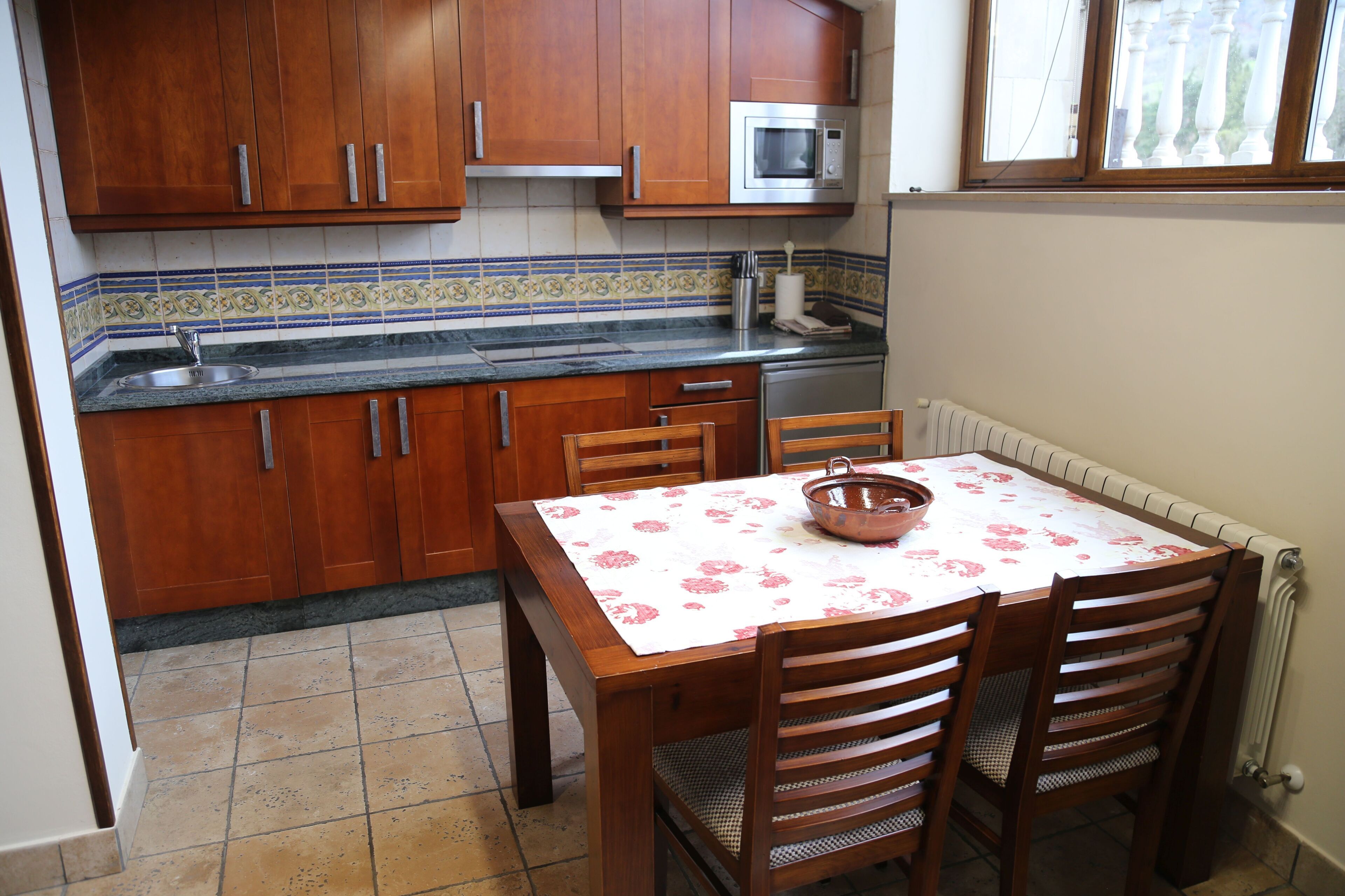 Una cocina con armarios de madera, microondas, pileta y una mesa de comedor con sillas.